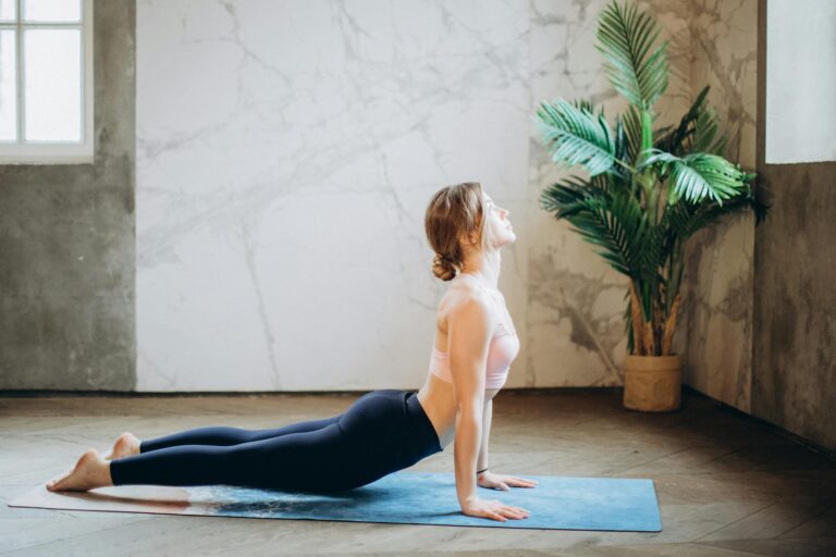 What is Surya Namaskar? Your Guide to Sun Salutations. 1 woman in pink sports bra and black leggings doing yoga on yoga mat