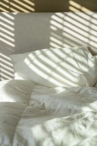Bed with pillows and sheets lit by patterned morning sunlight