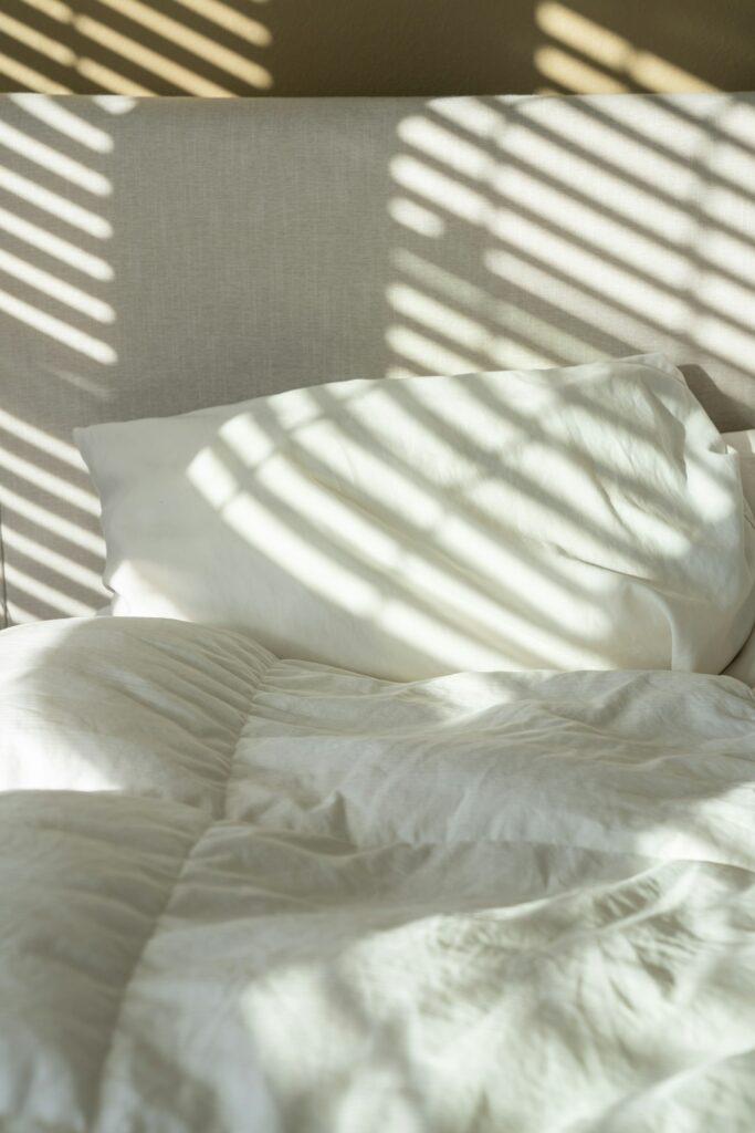 Bed with pillows and sheets lit by patterned morning sunlight
