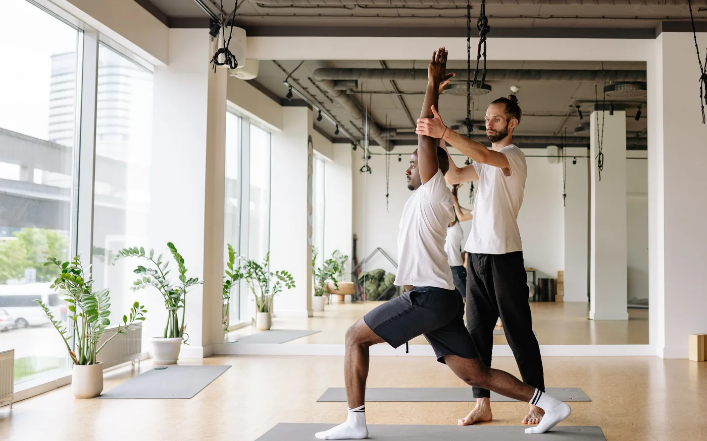 Yoga teacher guiding a student with alignment during an indoor practice